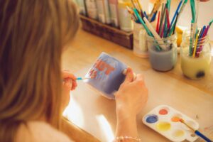 Close-up of a woman painting a mug in an art studio with bright colors.