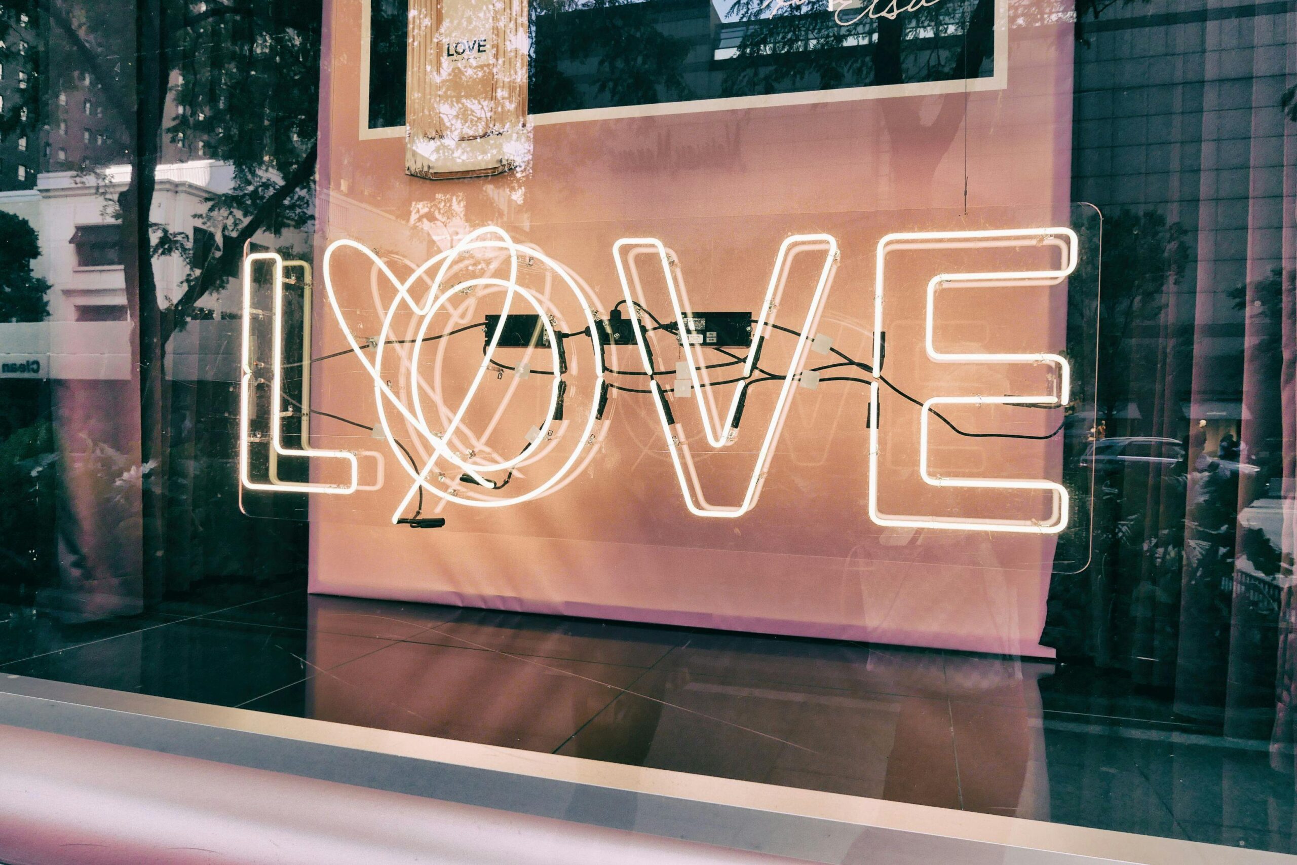 Neon 'LOVE' sign in a modern urban window display with reflections.